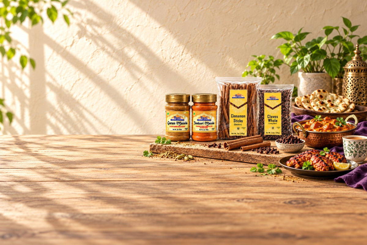 Rani Garam Masala, Tandoori Masala, Cinnamon Sticks and Cloves Whole on a sunlit kitchen table with butter chicken, naan, tandoori chicken and chai